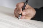 man's hand holding a pen writing his signature - plea bargain in federal court concept